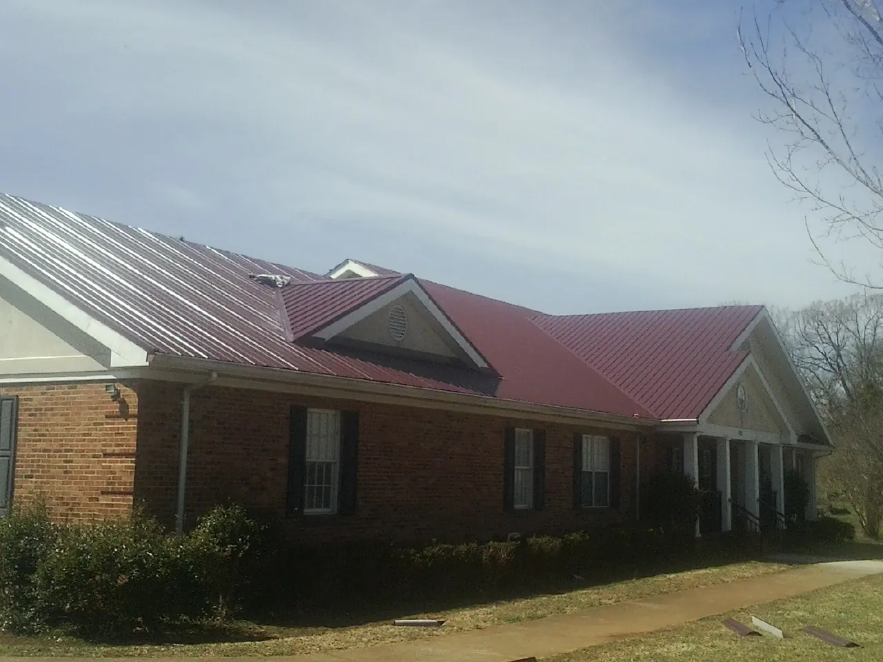 Red metal roof with gabled entries on a long brick building, from a Hail Damage Roof Repair job in Renovo
