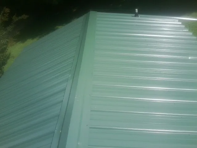 New green metal panels meeting at the ridge of a roof — Flat Roof Repair work by our crew in Renovo