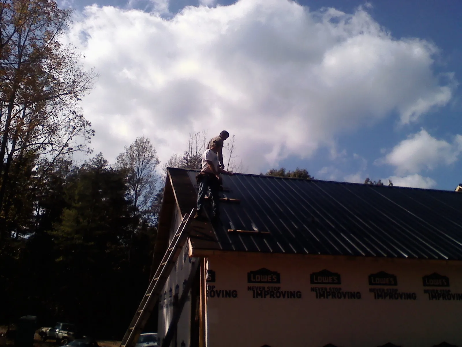 Roofer fastening dark metal panels high against a cloudy sky, from a Roof Inspection job in Renovo