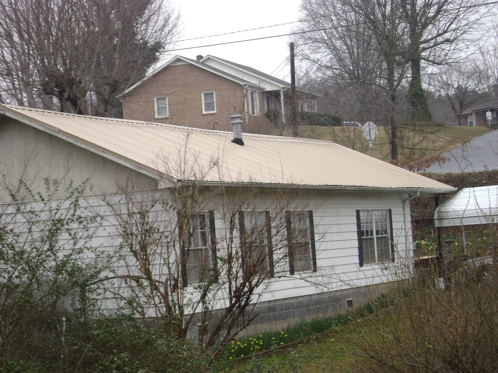 Tan metal roof on a white sided house set into a hillside — Commercial Roofing by Roofing Brothers in Renovo