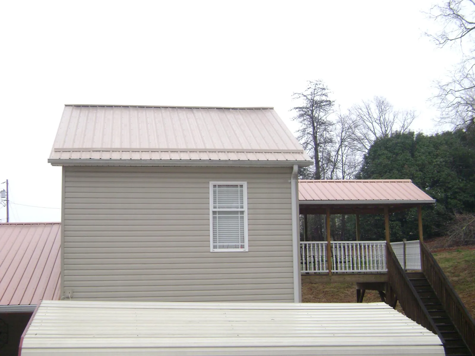 Tan metal roofs on a two story addition and attached porch, from a Roof Replacement job in Renovo